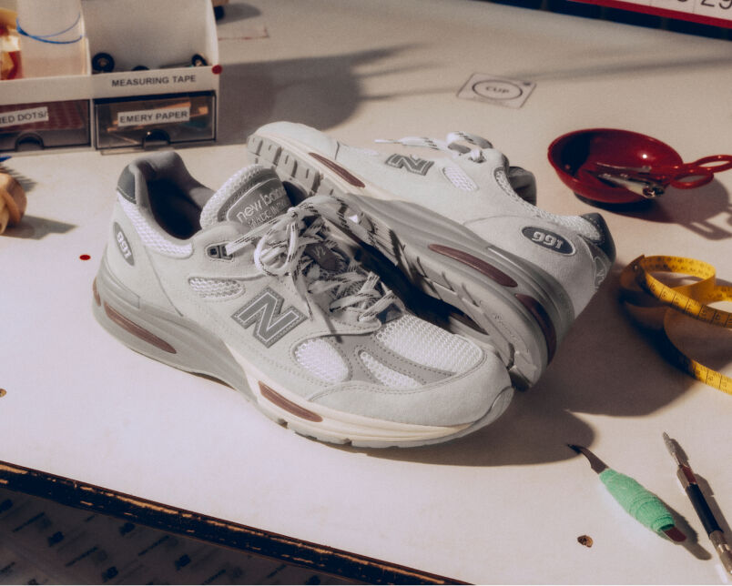 A pair of New Balance Made in UK sneakers on a white workbench surrounded by shoemaking tools and other textile equipment. 