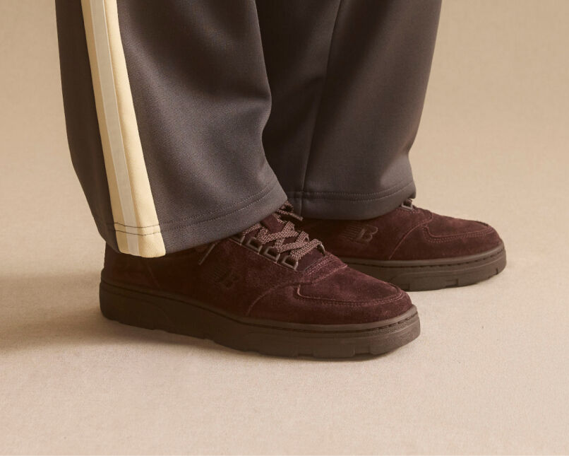 Knee down view of a man wearing a pair of New Balance Made in UK sneakers standing on a patterned tile floor.  