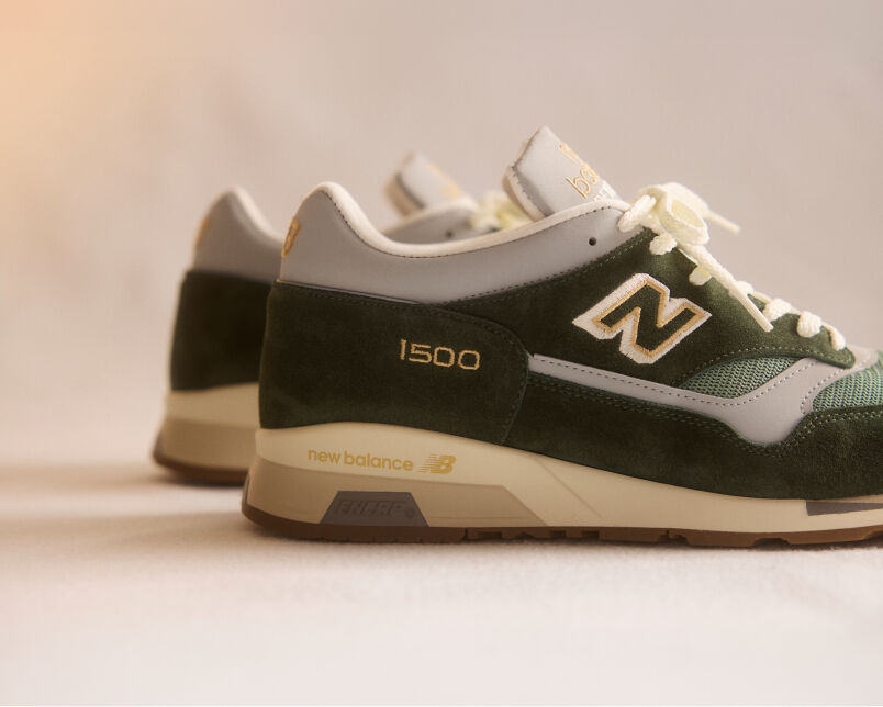 A pair of New Balance Made in UK sneakers on a green textured studio environment. 