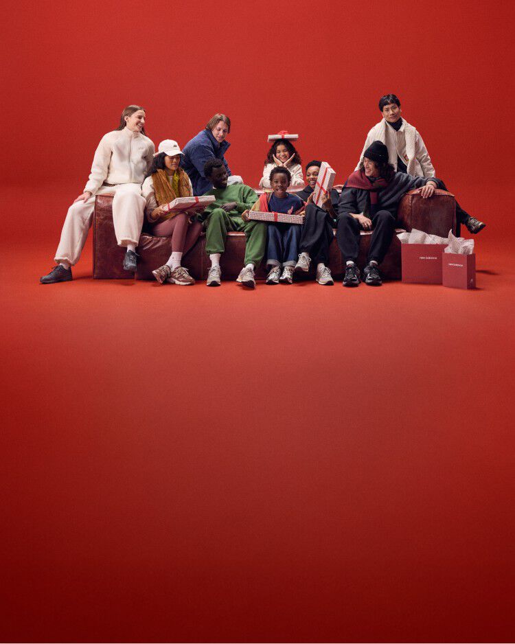 A group of people wearing New Balance sitting on a sofa with a red background.
